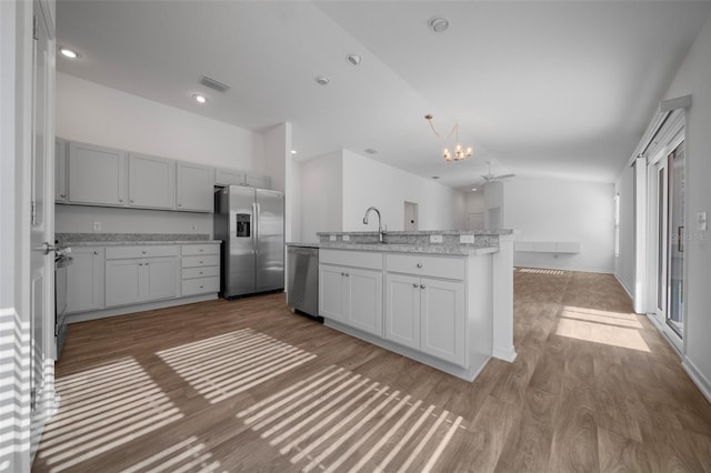 kitchen with lofted ceiling, light stone counters, a center island with sink, stainless steel appliances, and light hardwood / wood-style floors