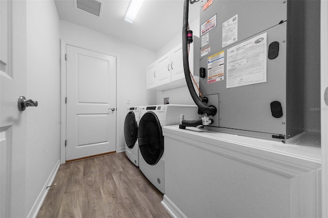 washroom featuring washer and dryer, cabinets, heating unit, and light wood-type flooring