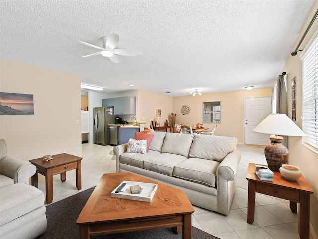 living room with ceiling fan, sink, a textured ceiling, and light tile patterned floors