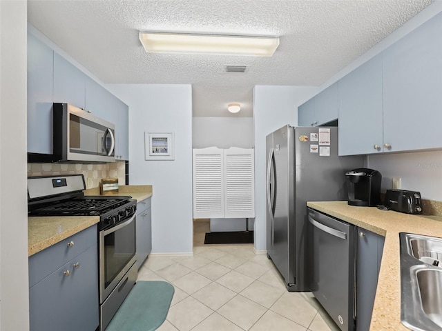 kitchen with backsplash, light tile patterned floors, blue cabinets, a textured ceiling, and stainless steel appliances