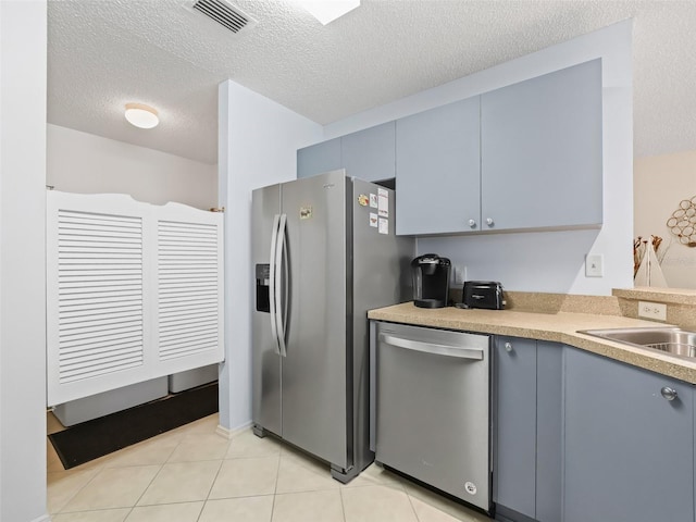 kitchen featuring light tile patterned floors, a textured ceiling, appliances with stainless steel finishes, and sink