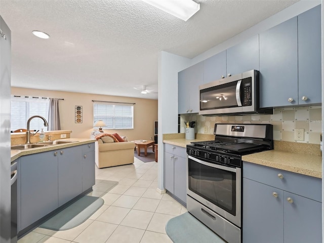 kitchen with appliances with stainless steel finishes, a textured ceiling, light tile patterned floors, decorative backsplash, and sink