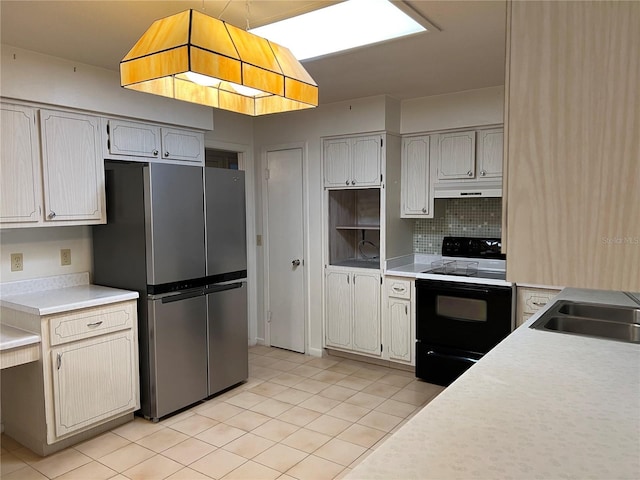 kitchen featuring light countertops, backsplash, freestanding refrigerator, under cabinet range hood, and black / electric stove