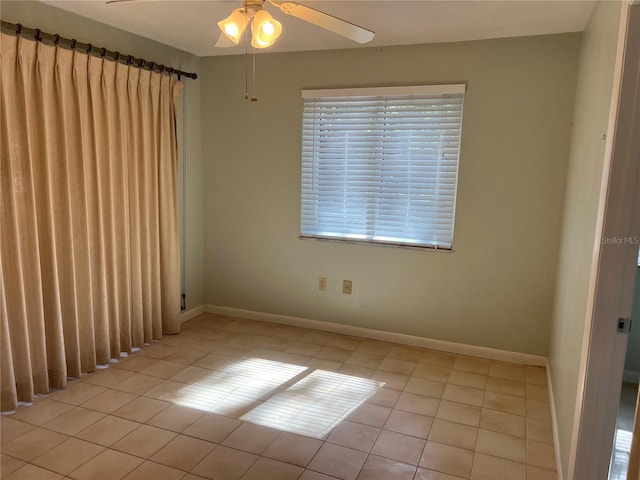 empty room with a ceiling fan, light tile patterned flooring, and baseboards