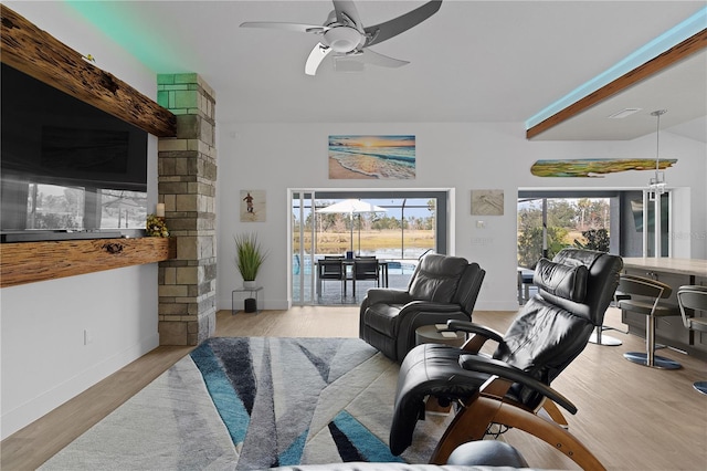 living room with a wealth of natural light, light hardwood / wood-style flooring, beamed ceiling, and ceiling fan