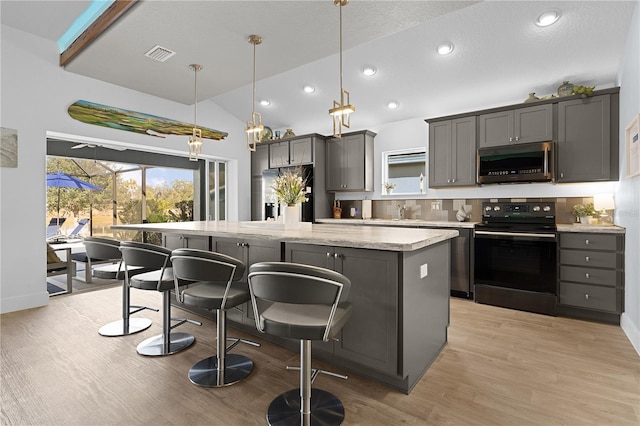 kitchen featuring vaulted ceiling, appliances with stainless steel finishes, hanging light fixtures, a center island, and light wood-type flooring