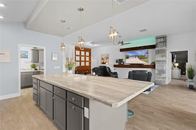 kitchen with a kitchen island, decorative light fixtures, gray cabinetry, a kitchen bar, and light hardwood / wood-style floors