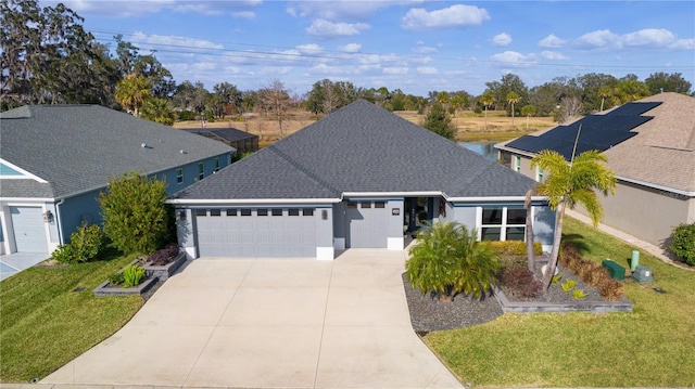 ranch-style house featuring a garage, roof with shingles, concrete driveway, and a front yard