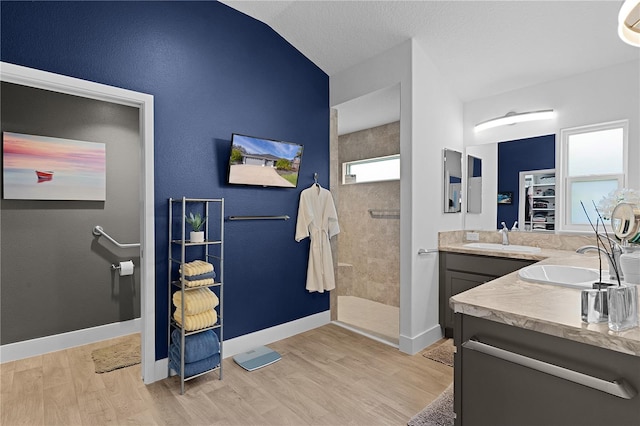 bathroom with hardwood / wood-style flooring, vaulted ceiling, tiled shower, and vanity