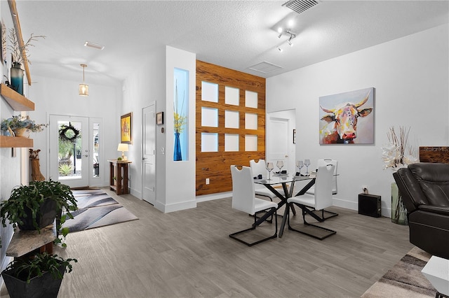 dining area featuring light wood-style flooring, wooden walls, visible vents, and a textured ceiling