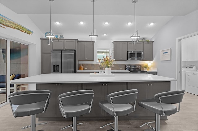 kitchen with lofted ceiling, stainless steel appliances, light countertops, gray cabinets, and washing machine and clothes dryer