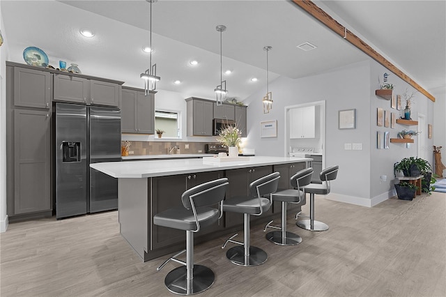 kitchen with a kitchen island, stainless steel appliances, light countertops, gray cabinetry, and a kitchen bar