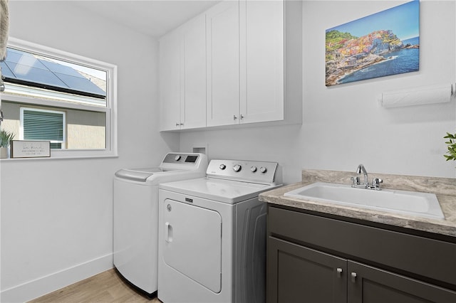 clothes washing area with light wood-style flooring, a sink, baseboards, cabinet space, and washing machine and clothes dryer