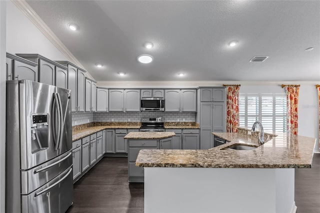 kitchen with gray cabinetry, stainless steel appliances, sink, a center island with sink, and crown molding