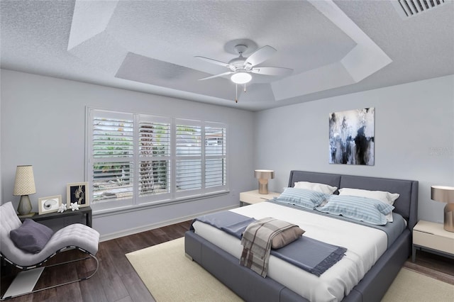 bedroom featuring ceiling fan, a textured ceiling, dark hardwood / wood-style flooring, and a raised ceiling