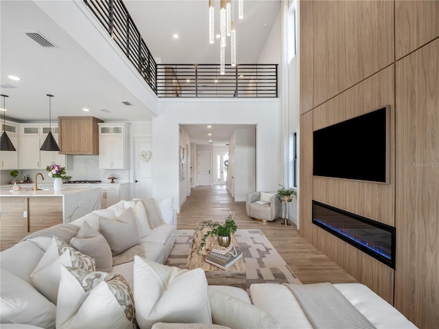 living room featuring a large fireplace, sink, a high ceiling, and light wood-type flooring