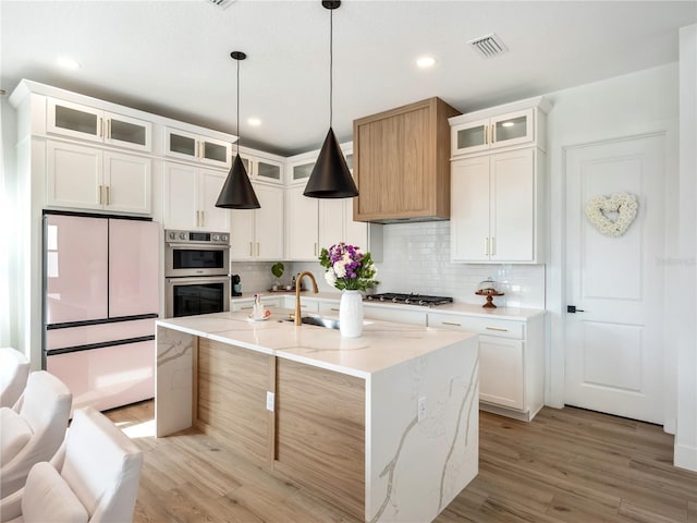 kitchen with white cabinetry, hanging light fixtures, a kitchen island with sink, and light stone counters