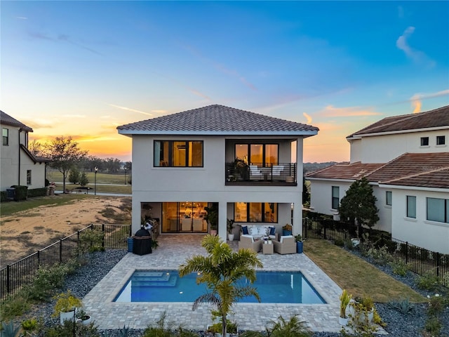 back house at dusk with an outdoor living space, a balcony, a fenced in pool, and a patio area