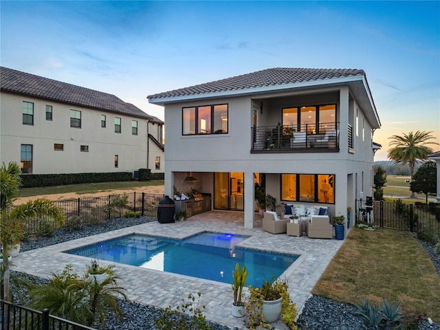 back house at dusk with a balcony, an outdoor living space, area for grilling, and a patio area