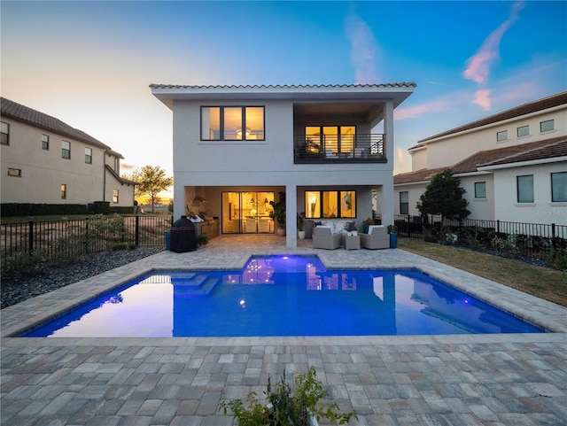 back house at dusk featuring an outdoor living space, a balcony, a fenced in pool, and a patio area