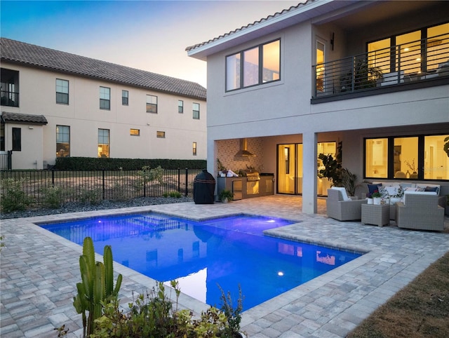 pool at dusk with a patio area, an outdoor hangout area, and an outdoor kitchen