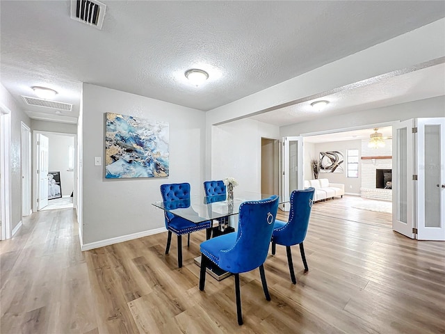 dining room with a brick fireplace, wood-type flooring, and a textured ceiling