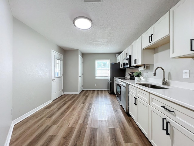 kitchen with appliances with stainless steel finishes, white cabinetry, sink, light wood-type flooring, and a textured ceiling