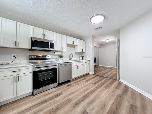 kitchen featuring white cabinetry, appliances with stainless steel finishes, light hardwood / wood-style floors, and a textured ceiling