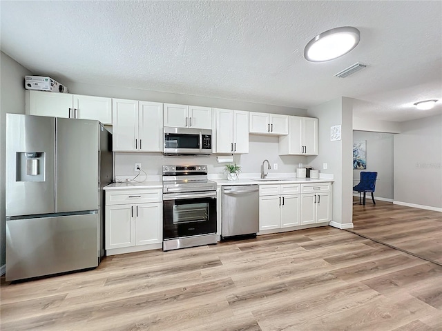 kitchen with appliances with stainless steel finishes, white cabinetry, sink, a textured ceiling, and light hardwood / wood-style flooring