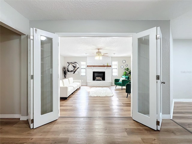 unfurnished living room featuring light wood-type flooring, ceiling fan, a brick fireplace, a textured ceiling, and french doors