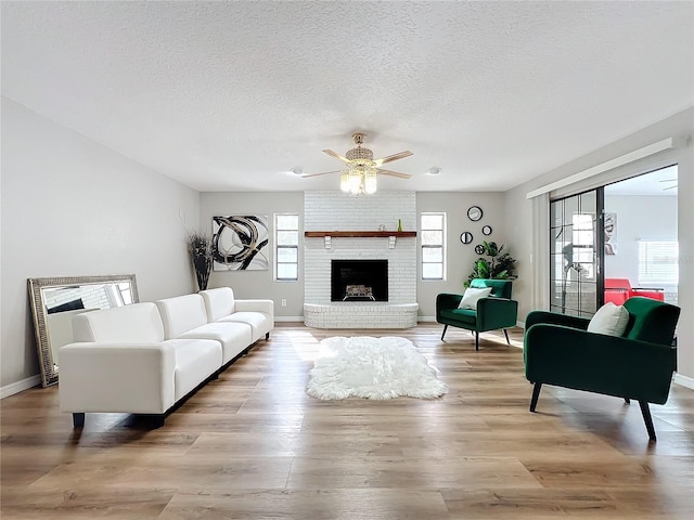 living room with ceiling fan, light hardwood / wood-style floors, a brick fireplace, and a textured ceiling