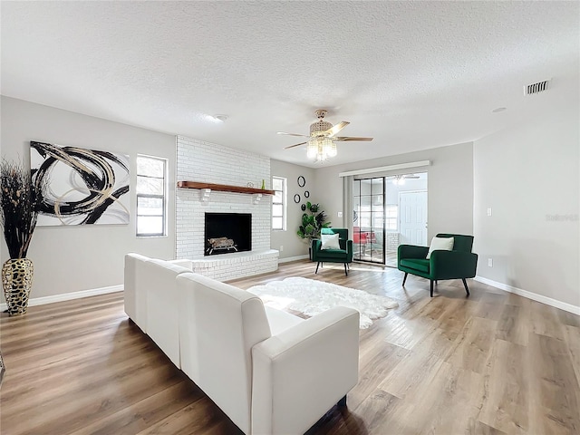 living room with hardwood / wood-style flooring, ceiling fan, a brick fireplace, and a textured ceiling