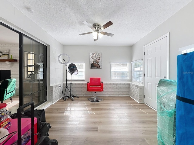 interior space featuring ceiling fan, brick wall, wood-type flooring, and a textured ceiling