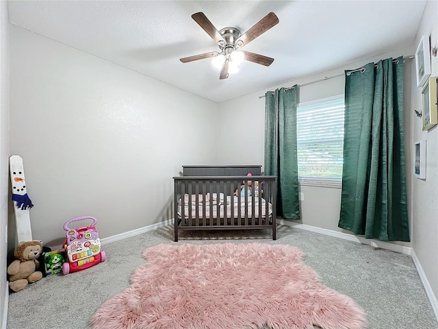 carpeted bedroom featuring a nursery area and ceiling fan