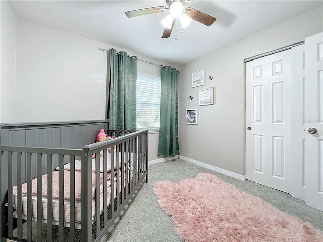 bedroom with a nursery area, light colored carpet, ceiling fan, and a closet