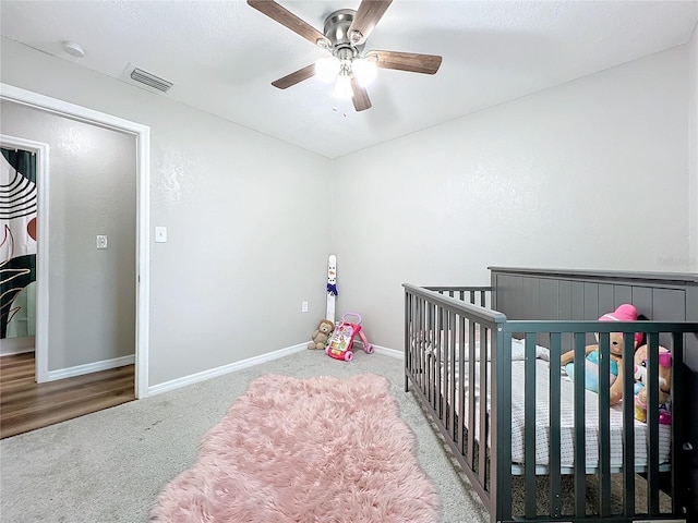 carpeted bedroom with a crib and ceiling fan