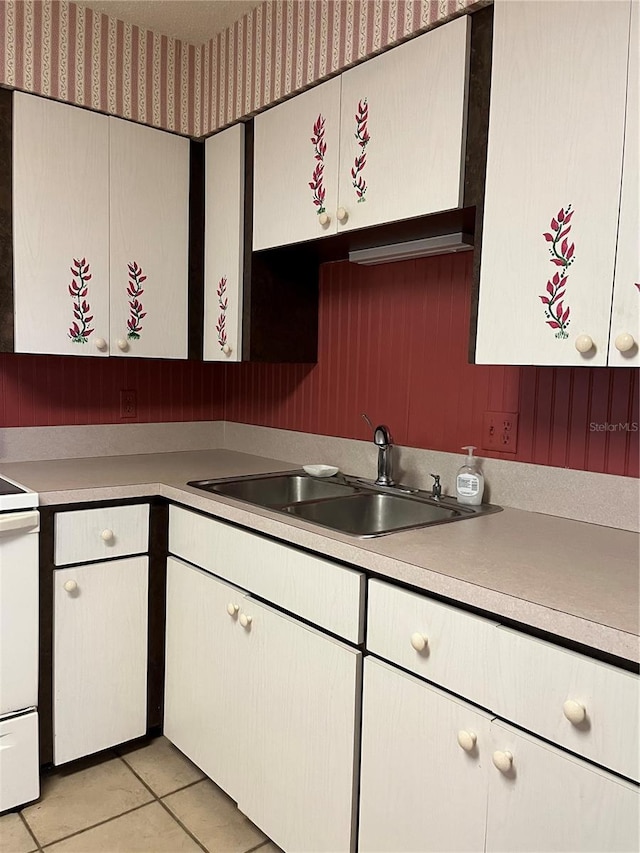 kitchen with white cabinetry, light tile patterned flooring, sink, and stove