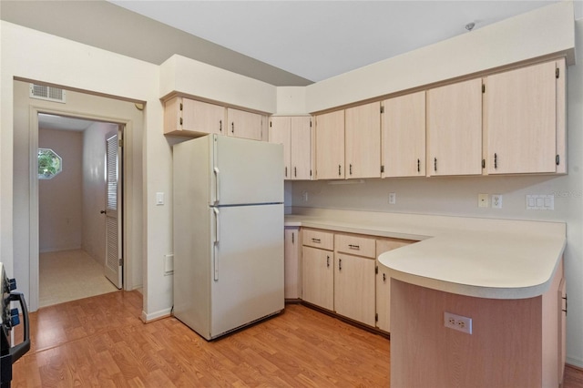 kitchen with light brown cabinetry, kitchen peninsula, white fridge, and light hardwood / wood-style flooring