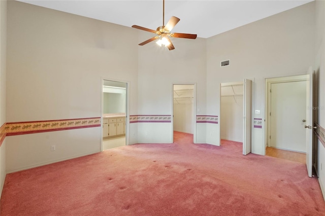 unfurnished bedroom featuring high vaulted ceiling, light colored carpet, ceiling fan, and ensuite bathroom