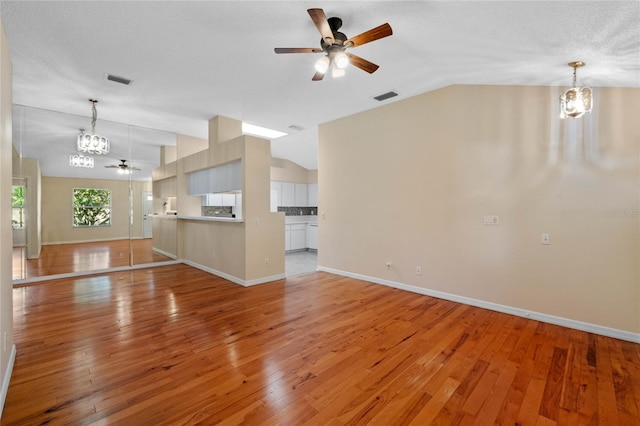 unfurnished living room featuring vaulted ceiling, ceiling fan with notable chandelier, and light hardwood / wood-style flooring