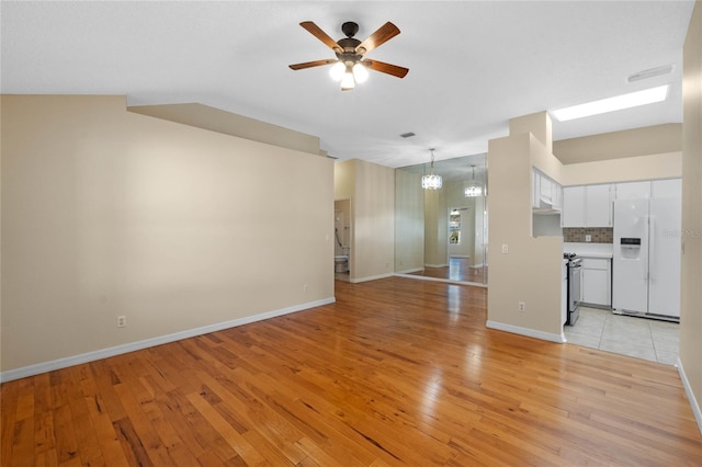 unfurnished living room with ceiling fan with notable chandelier and light hardwood / wood-style flooring