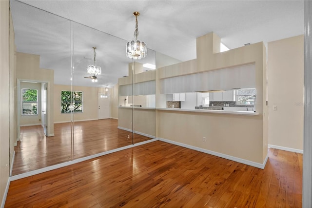 kitchen with pendant lighting, lofted ceiling, wood-type flooring, and ceiling fan with notable chandelier