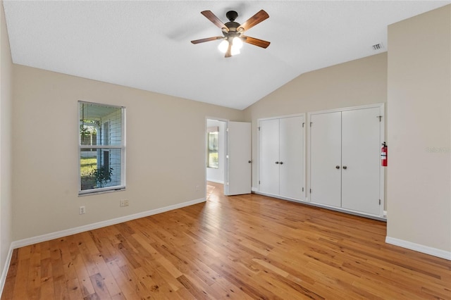 unfurnished bedroom featuring lofted ceiling, ceiling fan, light hardwood / wood-style floors, and multiple closets