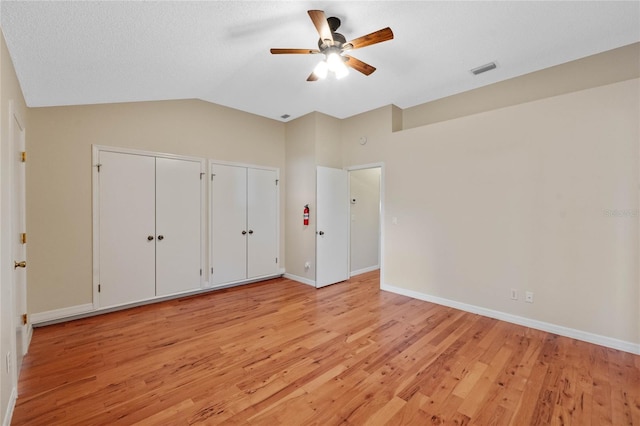 unfurnished bedroom featuring multiple closets, vaulted ceiling, ceiling fan, and light wood-type flooring