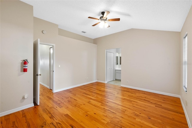 unfurnished bedroom with lofted ceiling, connected bathroom, a textured ceiling, light wood-type flooring, and ceiling fan