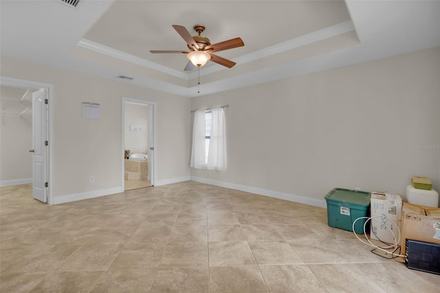 interior space with a walk in closet, ensuite bath, ornamental molding, a tray ceiling, and ceiling fan