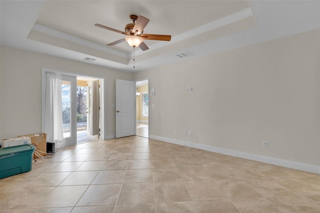 spare room with ceiling fan, ornamental molding, a tray ceiling, and light tile patterned floors