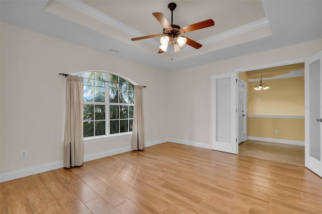 empty room with a raised ceiling, ornamental molding, ceiling fan with notable chandelier, and light hardwood / wood-style flooring