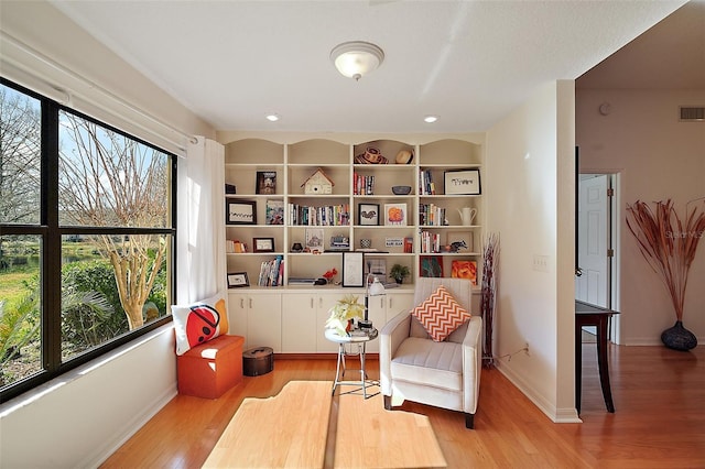 living area with built in shelves, plenty of natural light, and light hardwood / wood-style flooring