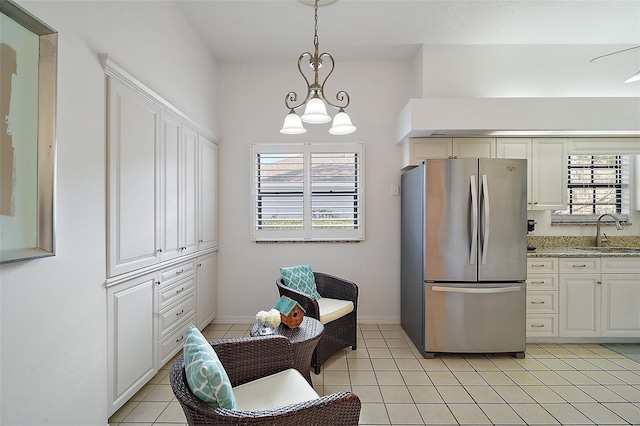 kitchen featuring decorative light fixtures, sink, stainless steel fridge, light tile patterned floors, and light stone countertops